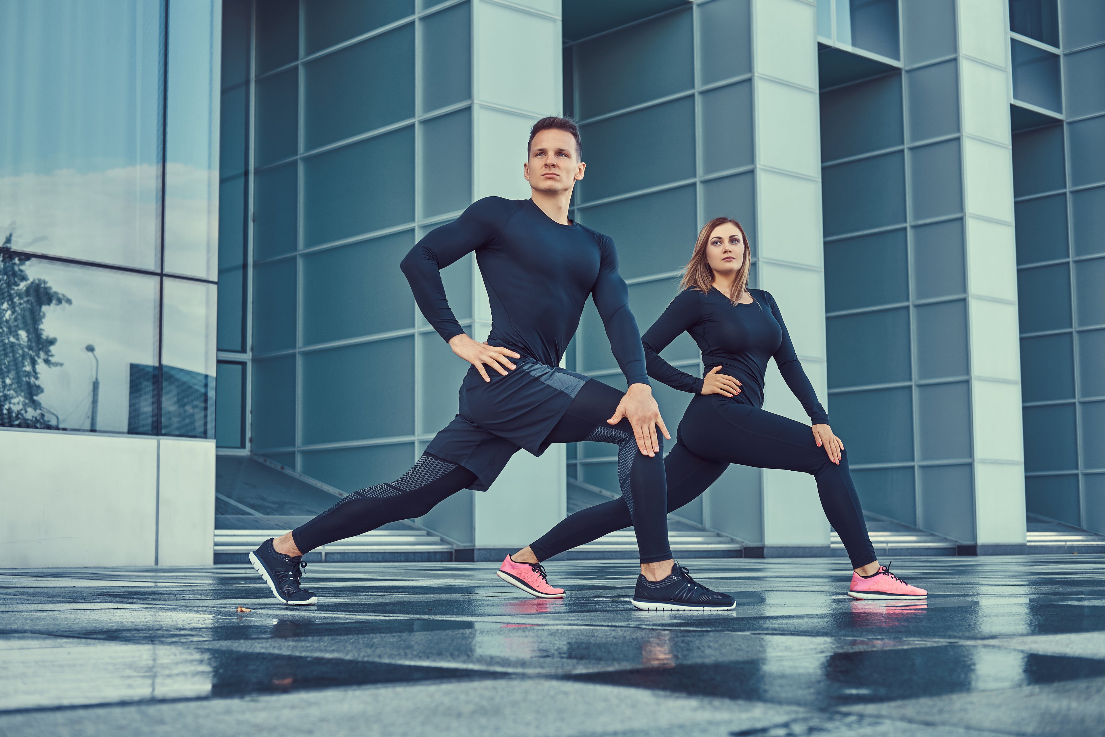 Two people in matching dark athletic wear standing in front of a modern building.